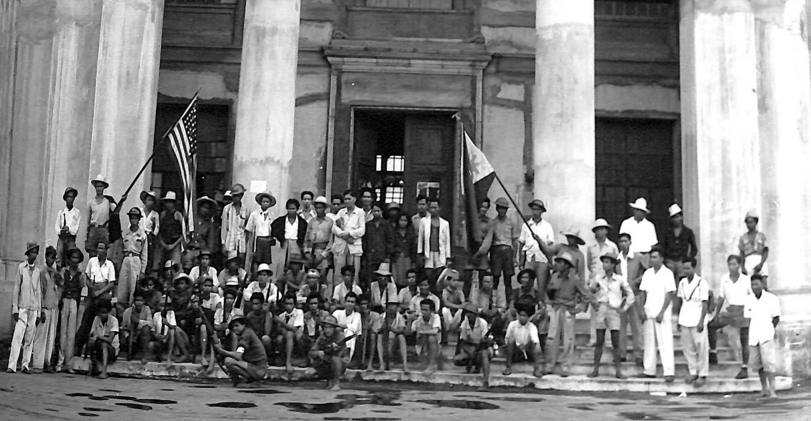 Photo of crowd in front of government building raising the American and Philippine flags