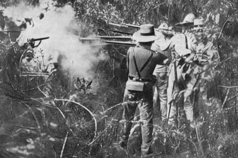 Black and white photo of soldiers firing rifles into jungle brush