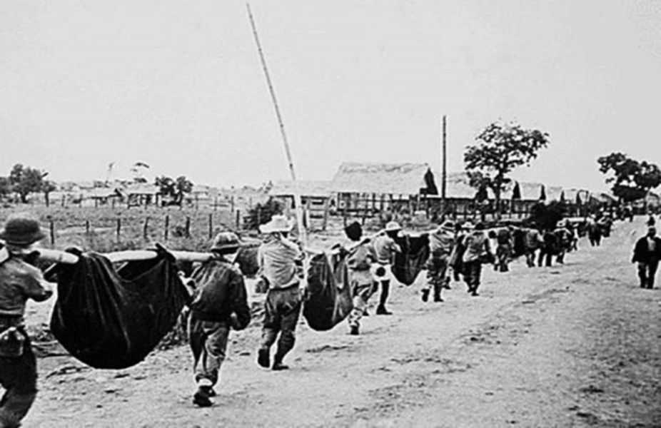Photo of men marching through a road carrying poles with sacks wrapped and hanging from them