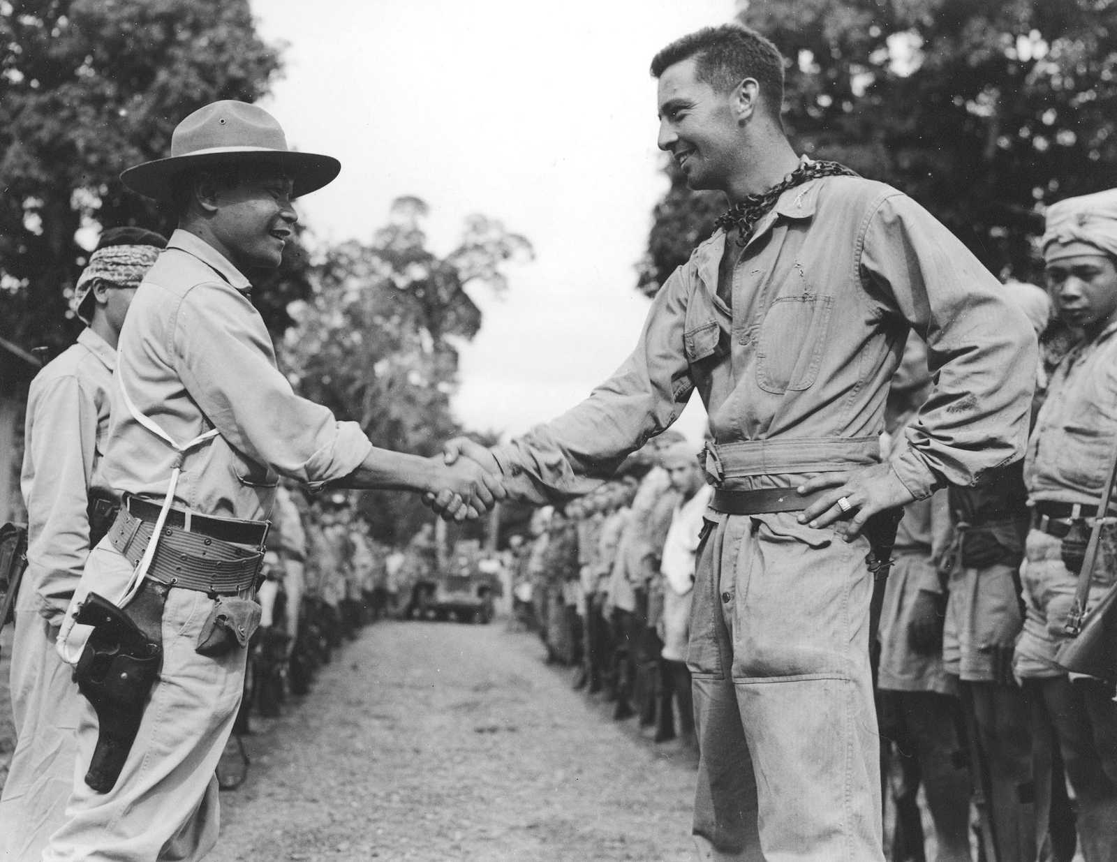 Photo of Filipino soldier shaking hands with an American, with other soldiers lined up beside them