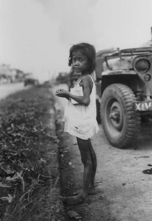 Photo of young Filipino child standing on a road with a military jeep behind her