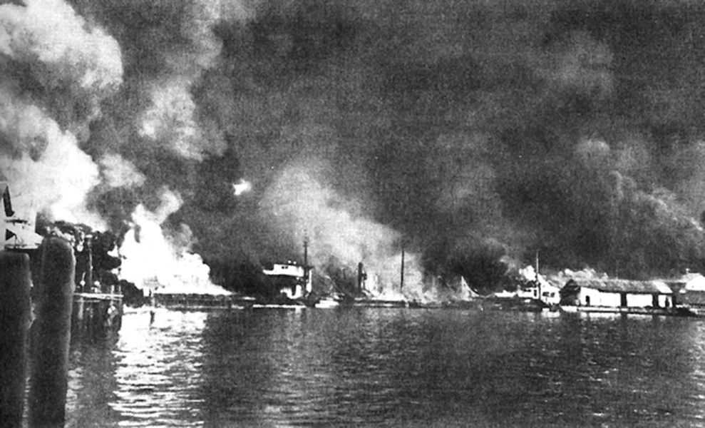 Photo of buildings burning along the coast of a body of water