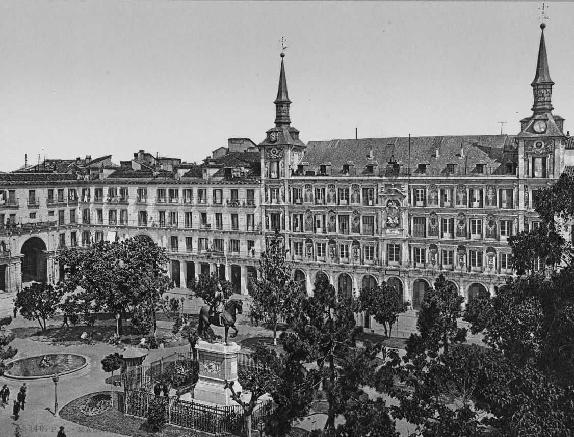 Black and white photo of Spanish buildings circling a plaza of trees and a sculpture
