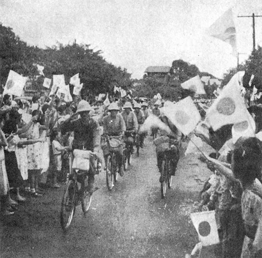 Photo of soldiers biking through crowd with Japanese flags waving around them