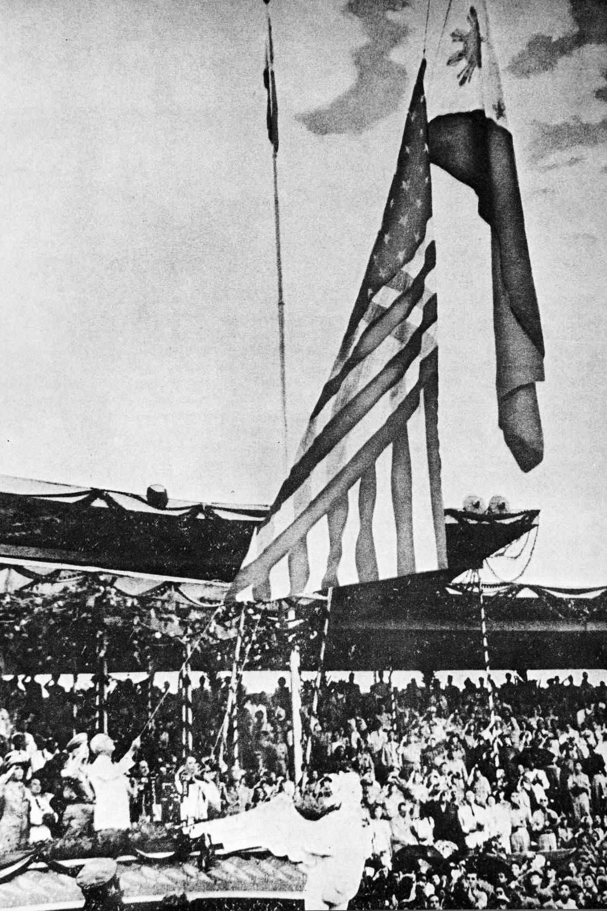 Photo of American flag being lowered while the Philippine flag raises over a crowd in a park