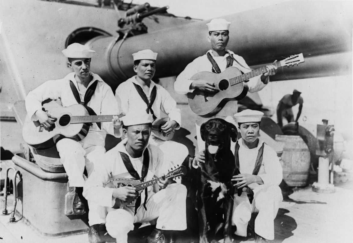 Photo of Filipinos in navy uniform holding instruments and posing with a dog