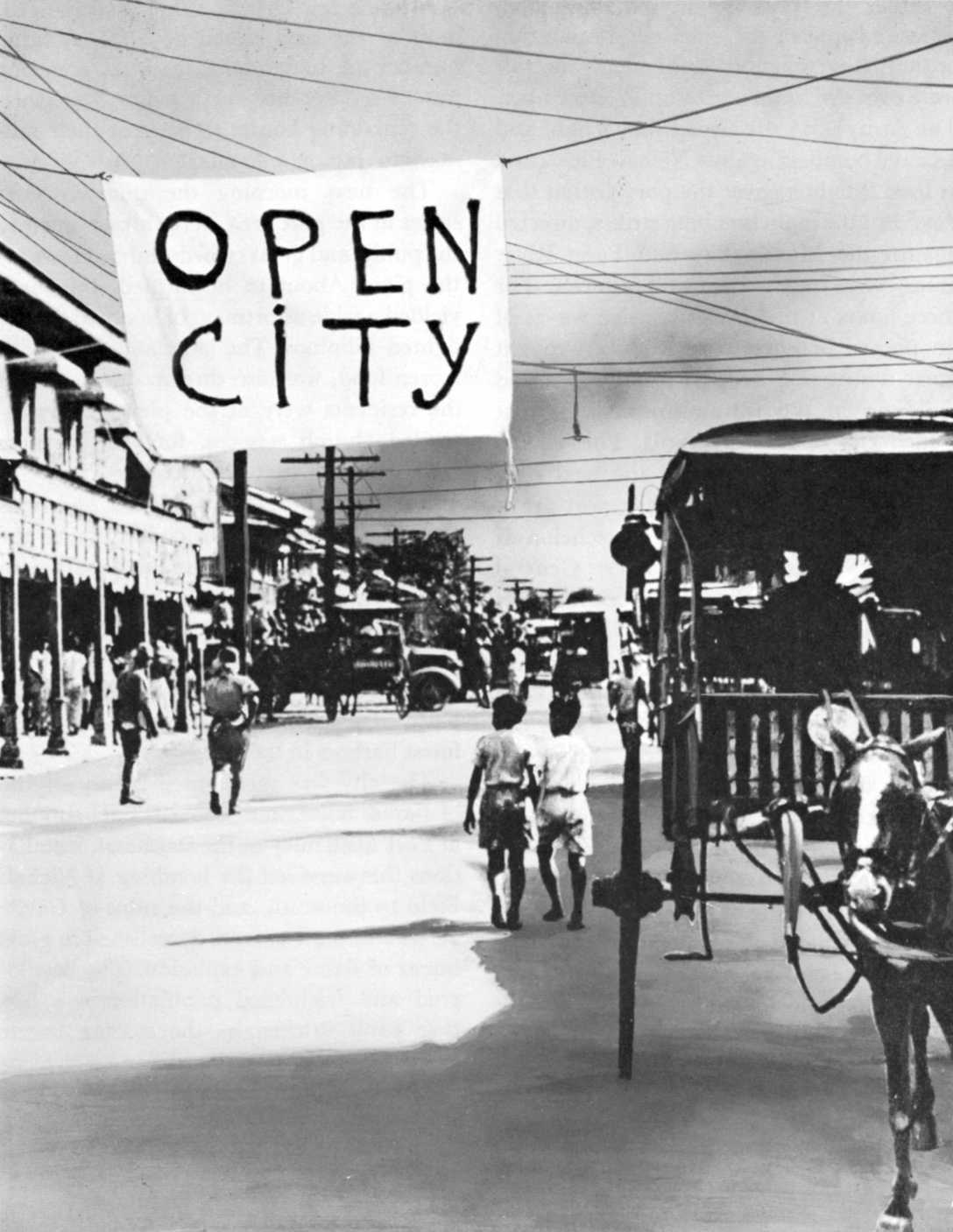 Photo of street in Manila with a sign reading OPEN CITY hanging above on a wire