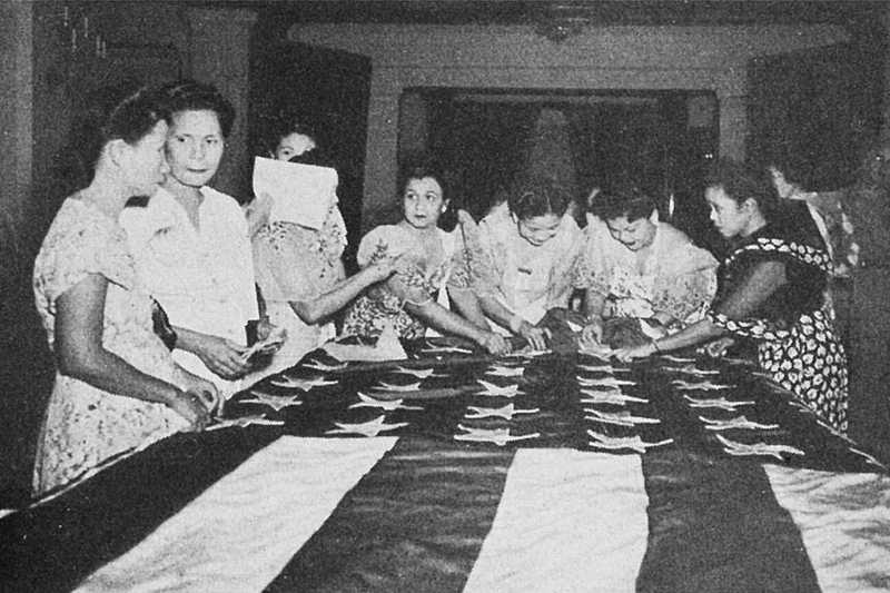 Photo of women standing over a cloth American flag, dewing and deliberating