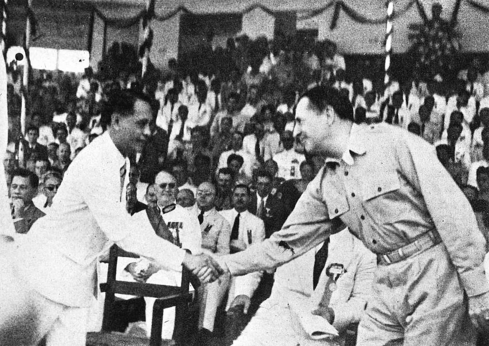 Photo of president Manuel Roxas shaking hands with Douglas MaxArthur in front of a crowd